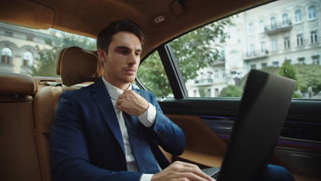 Portrait-of-focused-business-man-typing-on-laptop-computer-in-modern-car.