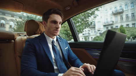 Angry-male-ceo-typing-laptop-computer-in-luxury-car.-Businessman-feeling-angry
