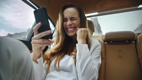 Portrait-of-happy-business-lady-getting-good-news-on-video-call-in-business-car.