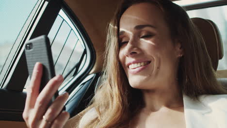 Freundliche-Geschäftsfrau-Lächelt-Bei-Einem-Videoanruf-Auf-Dem-Smartphone-In-Einem-Modernen-Luxusauto.