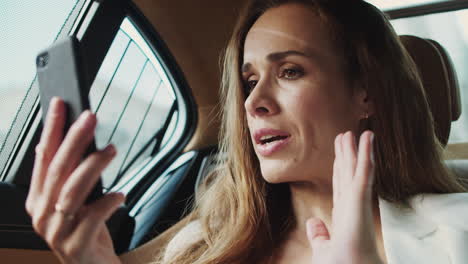 Portrait-of-anxious-business-lady-talking-in-video-chat-on-phone-in-modern-car.