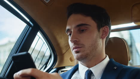 Portrait-of-young-business-man-writing-message-on-cellphone-in-modern-car.