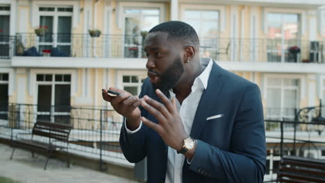 Irritated-african-man-talking-mobile-phone-outside.-Afro-guy-having-video-call