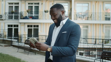 African-businessman-holding-cash-outside.-Cheerful-man-counting-money-outdoors