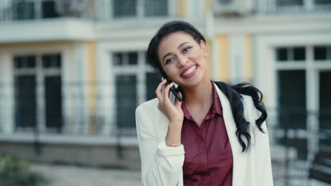Emotional-mixed-race-woman-laughing-on-phone-call-outdoors.-woman-talking-mobile