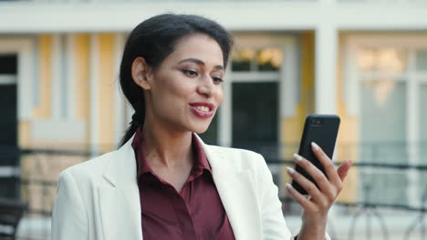 Smiling-mixed-race-woman-video-chatting-outside.-Lady-looking-phone-screen