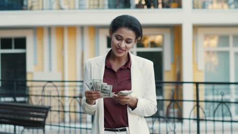 Cheerful-mixed-race-woman-counting-dollars-outside.-Businesswoman-keeping-cash