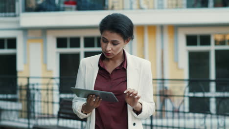 Focused-mixed-race-woman-scrolling-tablet-computer-outside.-Lady-reading-message