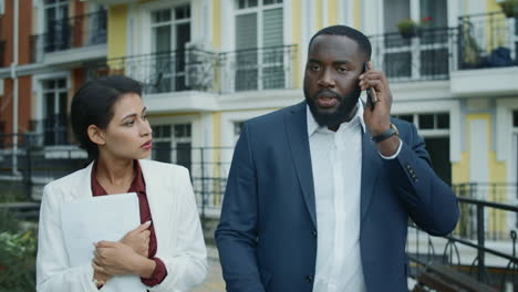 Mixed-race-man-and-woman-walking-outdoors.-Business-couple-calling-phone-outside