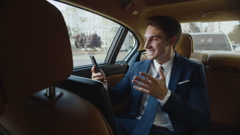 Joyful-business-man-telling-good-news-in-video-message-on-phone-in-business-car.
