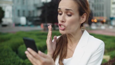 Annoyed-business-woman-swearing-by-video-call-on-smartphone-in-city-walk.