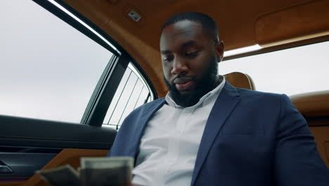 Portrait-of-businessman-counting-money-at-car.-African-guy-smelling-money-at-car