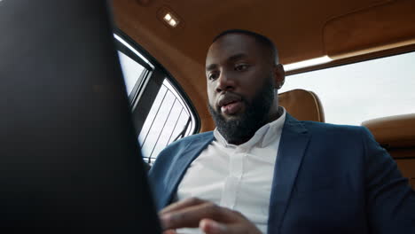 Closeup-afro-man-working-laptop-at-car.-Businessman-chatting-on-computer.