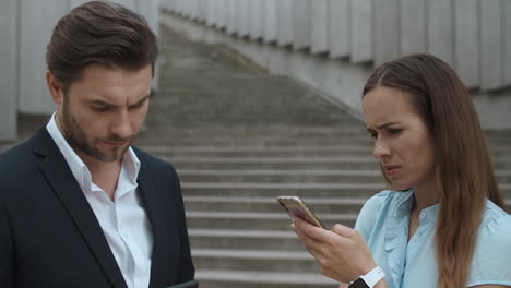 Man-and-woman-standing-on-street.-Business-couple-using-smartphones