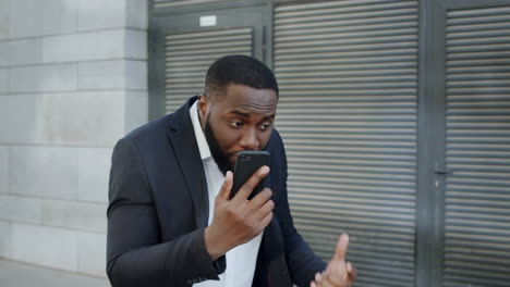 Afro-businessman-yelling-on-camera-at-street.-Manager-using-smartphone-outdoors