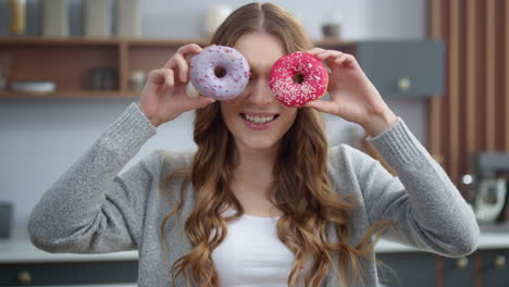 Smiling-woman-choosing-between-two-donuts-at-home.-Girl-having-fun-with-cakes.