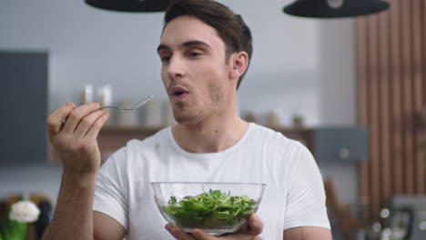 Smiling-man-eating-fresh-salad-at-home-kitchen.-Sporty-guy-enjoying-healthy-food