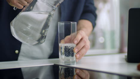 Closeup-male-hands-pouring-water-into-glass-from-jug-at-kitchen-background.