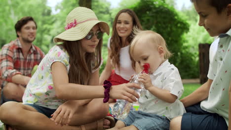Family-sitting-on-blanket-in-park.-Adorable-toddler-drinking-water-from-bottle