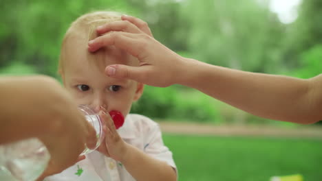 Mother-taking-care-about-son-outdoors.-Toddler-drinking-water-from-bottle