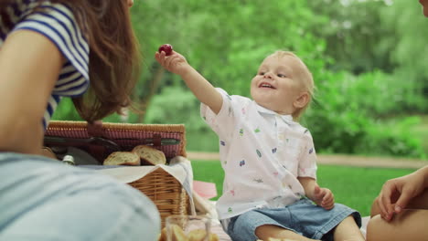Toddler-giving-cherry-to-mother-at-picnic.-Family-having-rest-in-forest-together