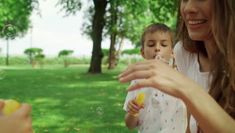 Woman-and-kids-playing-with-soap-bubbles.-Mother-and-children-sitting-on-blanket