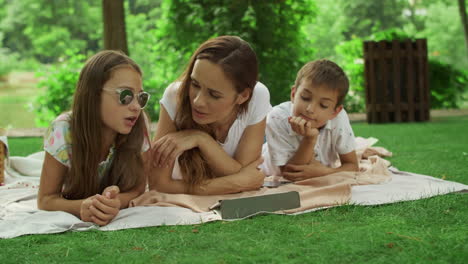 Mother-with-children-looking-at-tablet-screen-in-park.-Family-using-pad-outside