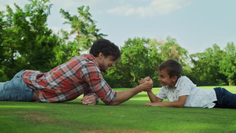 Father-and-son-lying-on-grass-in-field.-Boy-and-man-competing-in-arm-wrestling