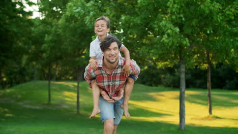 Boy-jumping-on-man-back-in-field.-Portrait-of-happy-father-carrying-son-on-back
