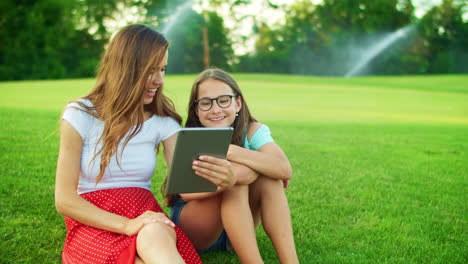 Cute-girl-and-woman-waving-hands-at-camera-on-digital-tablet-outdoors