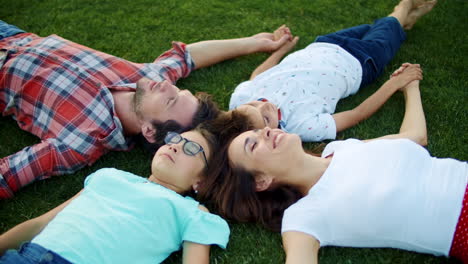 Family-lying-in-circle-on-grass-outdoors.-Parents-and-children-holding-hands
