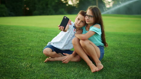 Sister-hugging-brother-in-park.-Smiling-boy-taking-selfie-on-cellphone-with-girl