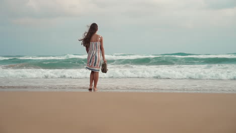 Young-woman-looking-to-storm-at-seashore.-Happy-teenager-walking-in-sea-surf.