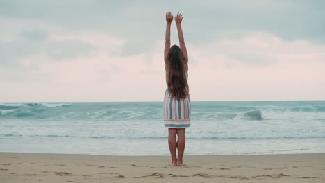 Young-woman-raising-arm-at-seaside.-Carefree-girl-enjoying-sunrise-at-beach.
