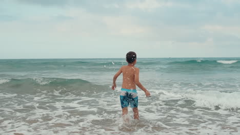 Happy-boy-enjoying-summer-at-beach.-Cheerful-boy-jumping-in-waves-at-seaside.