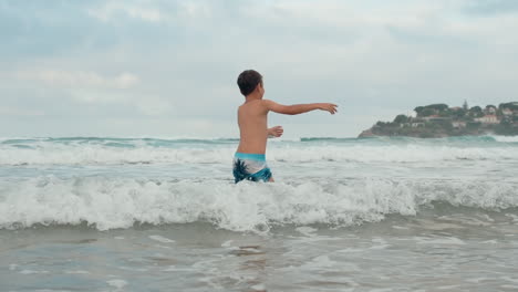 Happy-boy-having-fun-at-coastline.-Carefree-guy-dancing-in-water-at-seashore.