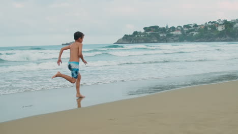 Cheerful-boy-enjoying-summer-activities-at-beach.-Guy-running-along-sea-surf.