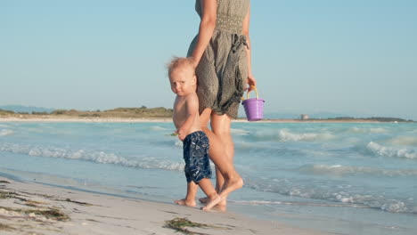 Cute-child-looking-around-at-seashore.-Baby-boy-walking-with-mother-at-beach.