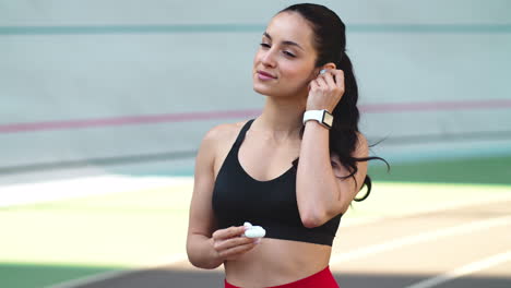 Mujer-Deportiva-Usando-Auriculares-En-La-Pista-Moderna.-Mujer-En-Forma-Escuchando-Música-Al-Aire-Libre.