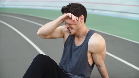 Close-up-of-exhausted-man-sitting-on-stadium-track.-Sport-man-resting