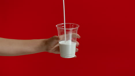 Wide-view-of-woman-hands-pouring-milk-into-empty-plastic-glass-in-slow-motion.