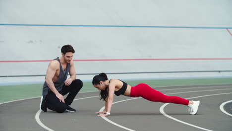 Mujer-Haciendo-Flexiones-En-El-Estadio-Deportivo.-Pareja-Entrenando-Juntos-En-El-Estadio-Deportivo