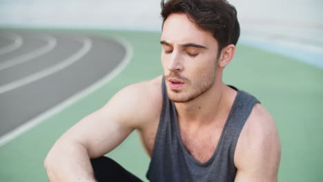 Athlete-man-resting-after-workout-at-stadium.-Tired-runner-sitting-on-racetrack