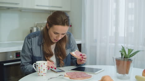Smiling-woman-talking-smartphone-during-breakfast-in-modern-kitchen.