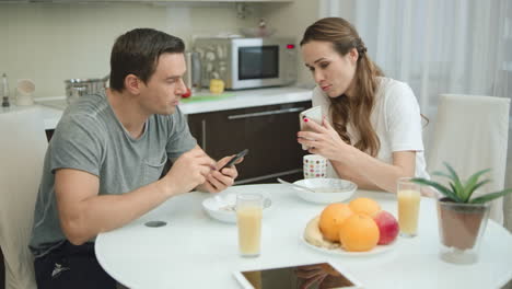 Happy-couple-looking-mobile-phones-during-healthy-breakfast.
