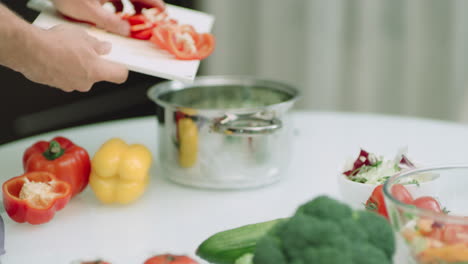 Closeup-man-hands-putting-sliced-peppers-into-cooking-pot-in-slow-motion.