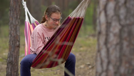 Female-teenager-swinging-in-hammock-with-joyful-mood-in-forest.