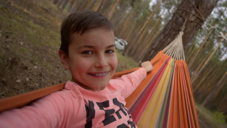Portrait-of-teenage-boy-smiling-in-swinging-hammock-in-forest.