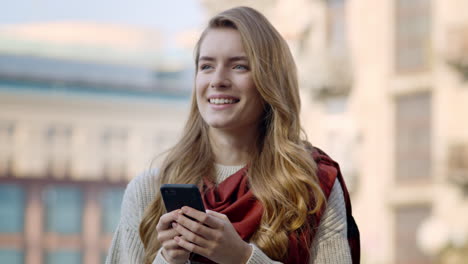 Joyful-girl-using-phone-outdoors.-Smiling-woman-standing-with-phone-on-street.