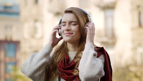 Joyful-woman-listening-music-headphones-on-street.-Happy-girl-using-earphones.